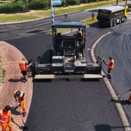 Asfaltploeg van Versluys Wegenbouw brengt met een asfaltspreidmachine een nieuwe asfaltlaag aan op een weg.